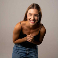 Thumbnail for Smiling woman with long brown hair wearing a black top and denim jeans, expressing joy and happiness.