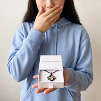 Thumbnail for Moved woman in a blue hoodie holding the Brother & Sisters gift box with the black clover photo necklace inside | SKU: TPH-CLVN-BLACK