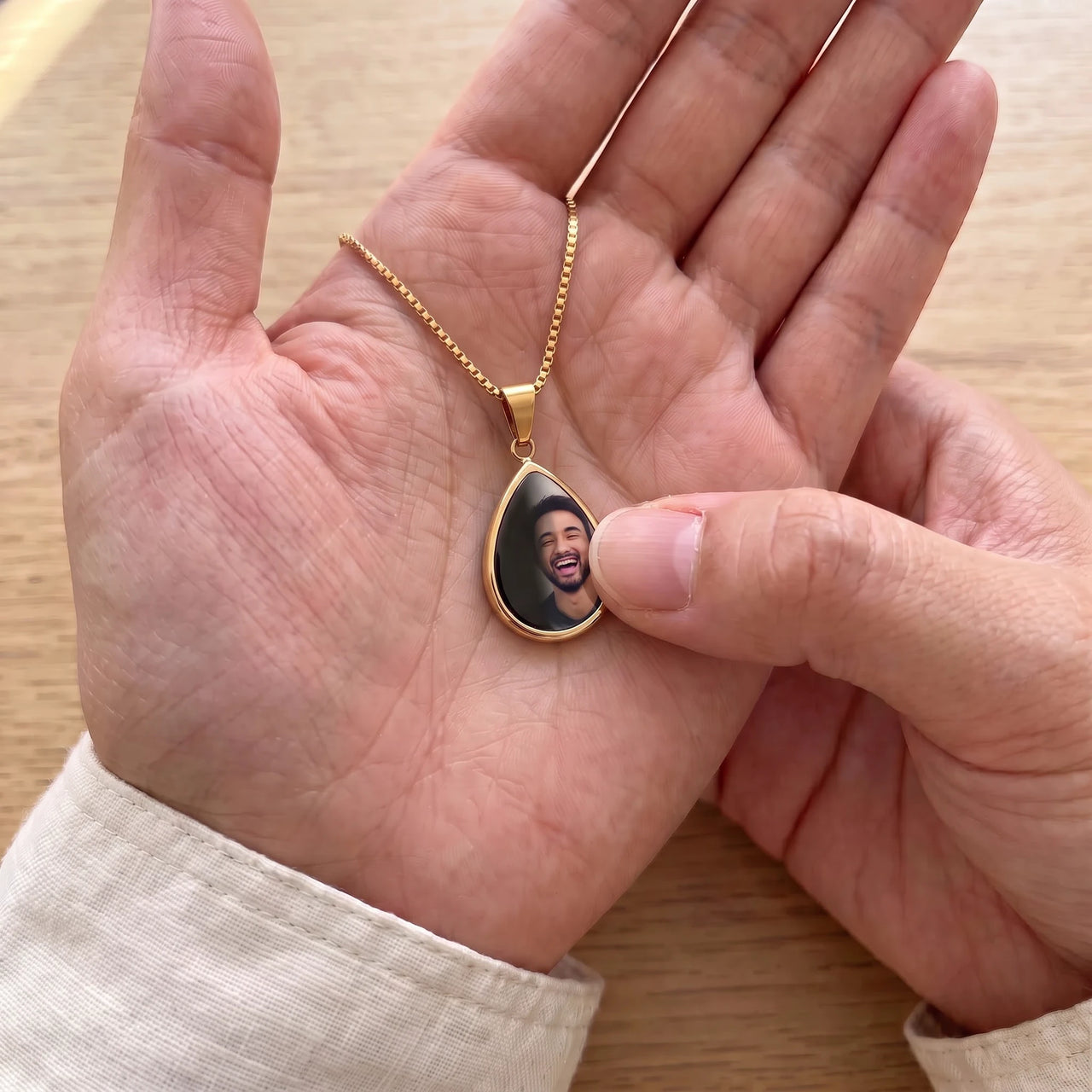 Thumb warming the gold teardrop pendant: the hidden photo appears under the thumb while the rest stays black | SKU: TPH-DRPN-GOLD