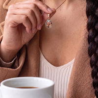 Thumbnail for Woman touching the gold teardrop pendant to reveal the photo, a cup of coffee in front of her | SKU: TPH-DRPN-GOLD
